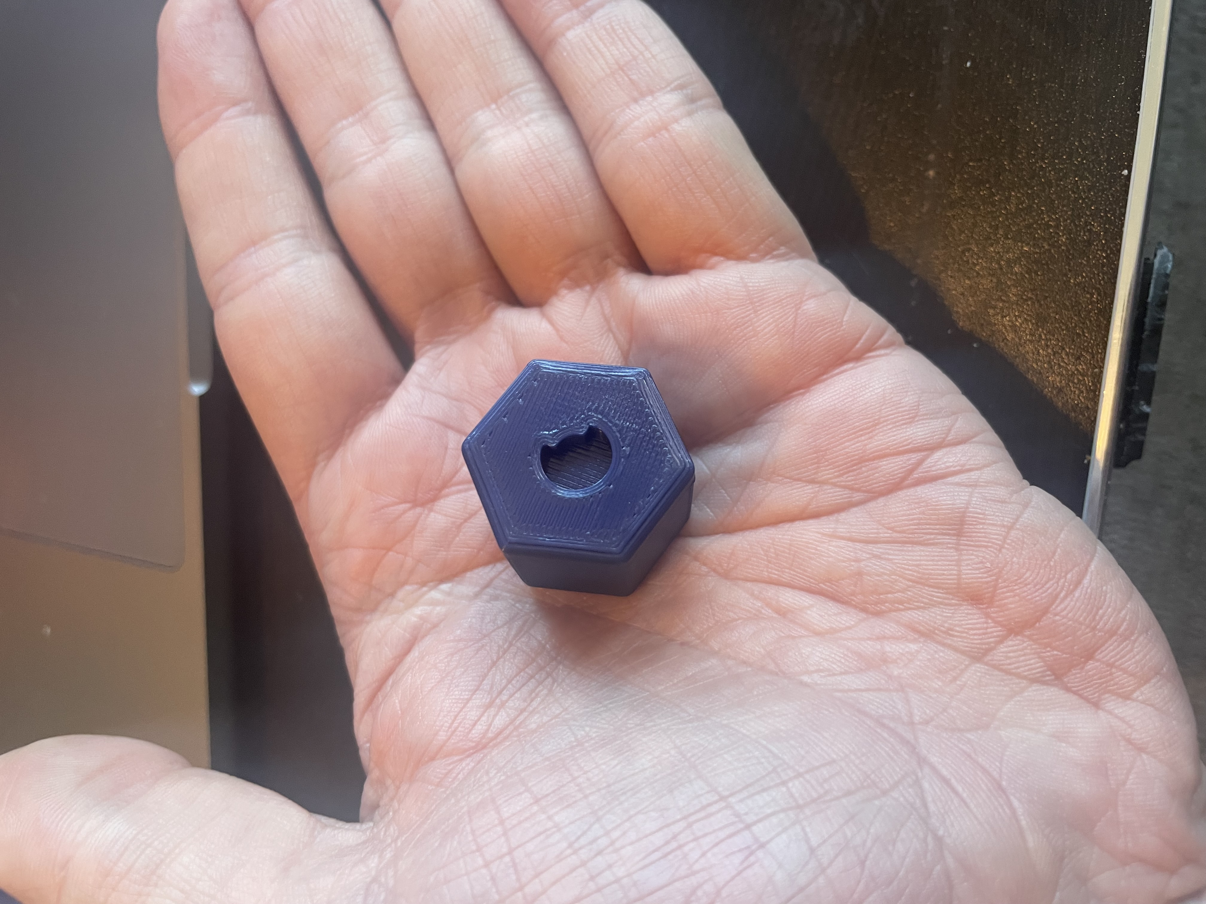 The finished token, held in the palm — filleted hexagonal prism with C groove on the top face